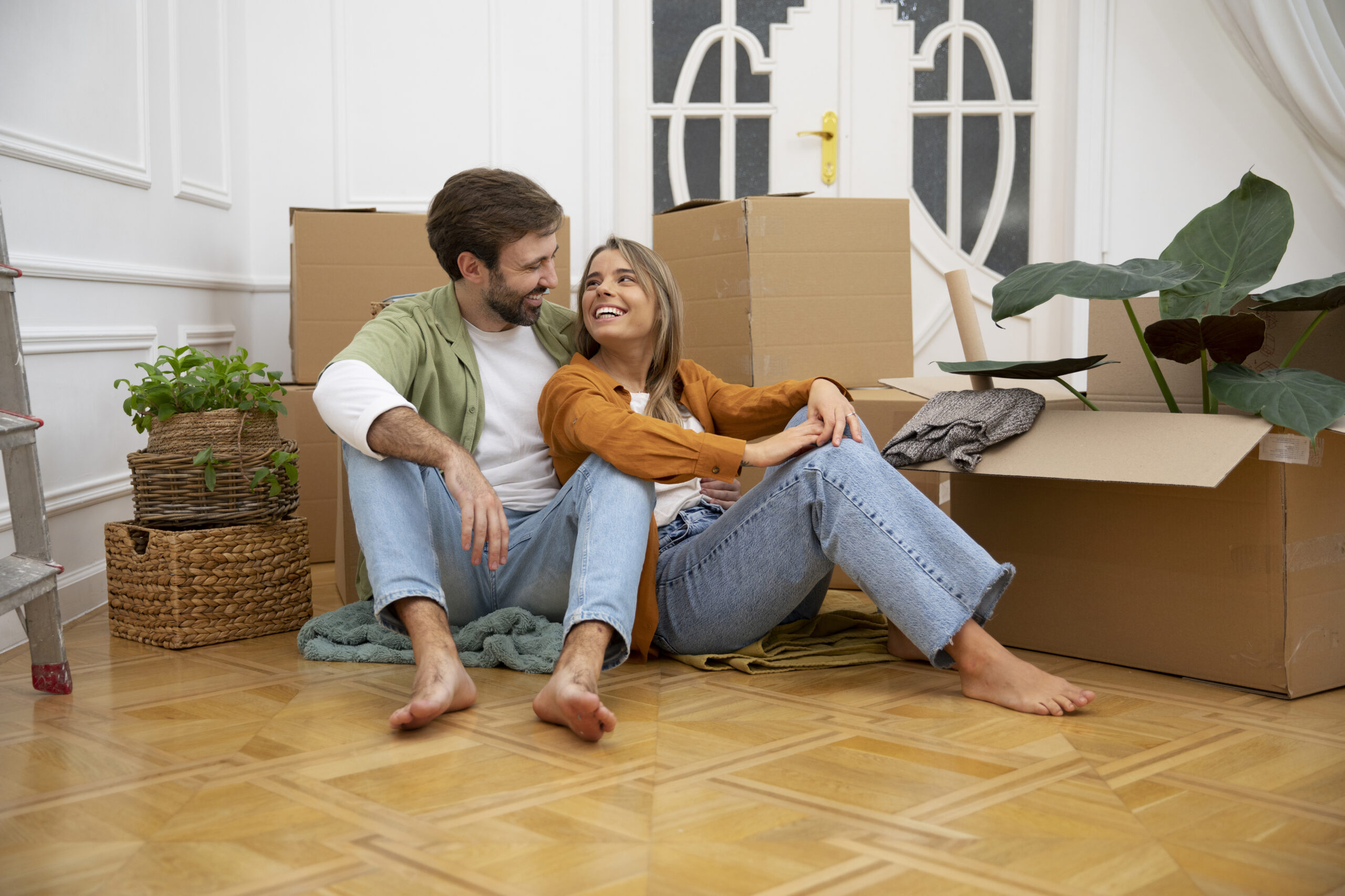 Couple sitting together in their new home, surrounded by cardboard moving boxes.